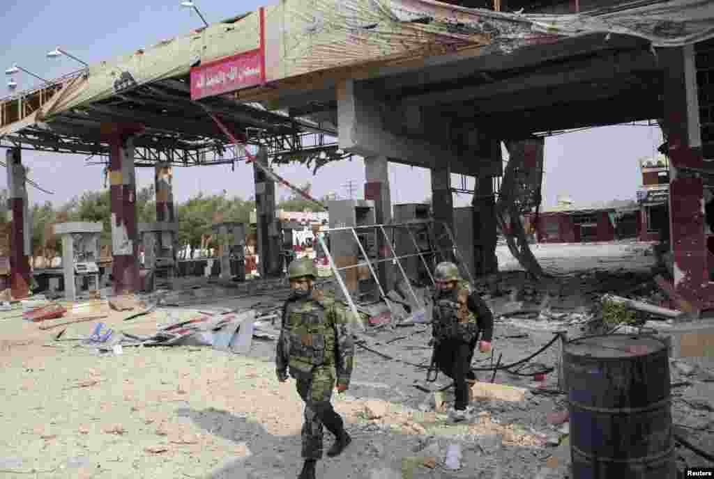Forces loyal to Syria's President Bashar al-Assad walk near a damaged gas station near the main highway leading Aleppo to Raqqa, Nov. 11, 2013.