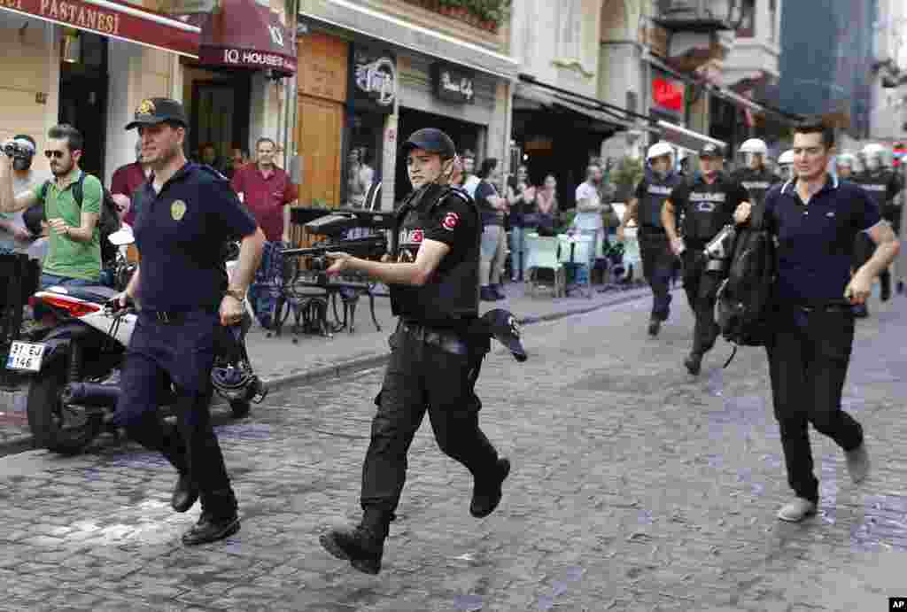 Polisi Turki, salah satunya memegang senapan peluru karet, berlari membubarkan peserta pawai Gay Pride di Istanbul (28/6). (AP/Emrah Gurel)