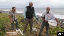 FILE - A Malaysian expert, center, looks for debris from the ill-fated Malaysia Airlines flight MH370 on a beach in Saint-Andre de la Reunion, on Reunion Island, in the Indian Ocean, Aug. 4, 2015. 