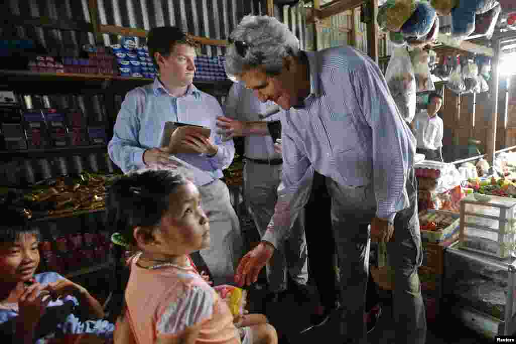 U.S. Secretary of State John Kerry gives a bag of cookies to children in a shop in Kien Vang along the Mekong River Delta, Dec.15, 2013.