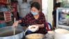អ្នកស្រី ពិន នារី លក់​គុយទាវ​ឆា និង​បបរ​នៅ​កែង​ផ្លូវ​មួយ​ជិត​ស្នាក់ការ​សង្កាត់​ចតុមុខ ដែល​បាន​ផ្អាក​ជាង​មួយ​ខែដោយសារ​ជំងឺ​កូវីដ​១៩ កំពុង​បើក​លក់​ឡើង​វិញ នៅថ្ងៃទី២៧ ខែមេសា ឆ្នាំ២០២០។ (កាន់ វិច្ឆិកា/VOA)