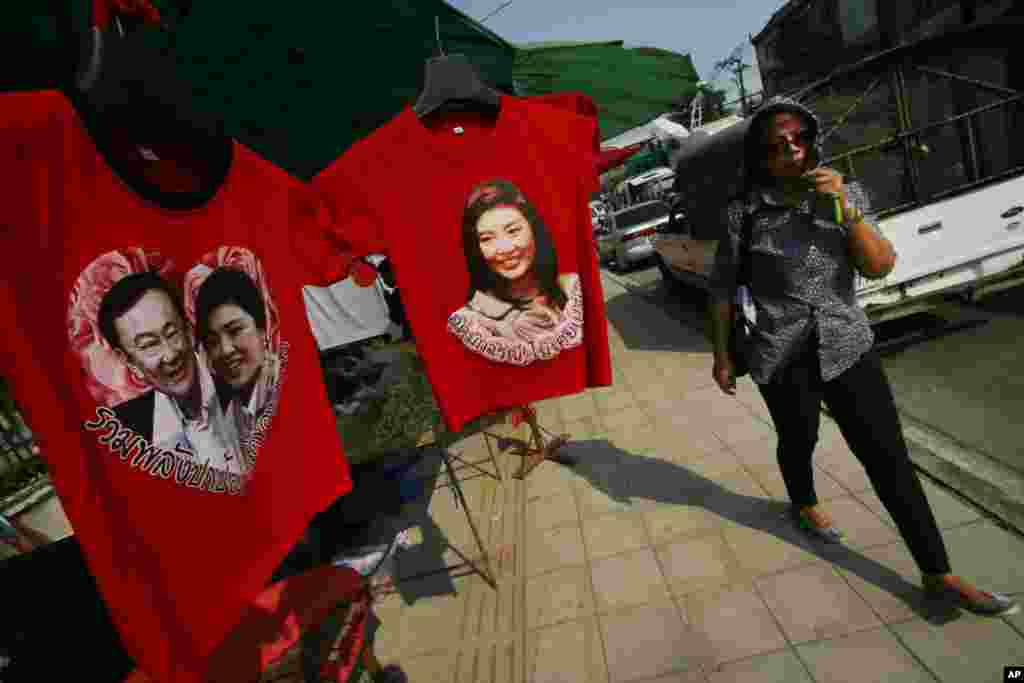 A pro-government supporter passes t-shirts with portraits of Prime Minister Yingluck Shinawatra and her self-exiled brother Thaksin at the gate of the National Anti-Corruption Commission office in Bangkok, Feb. 27, 2014. 