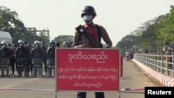 A policeman stands by a sign reading "If this line is crossed, Myanmar police force will fire with live ammunition" during a protests against the military coup in Naypyitaw, Myanmar, Feb. 8, 2021.