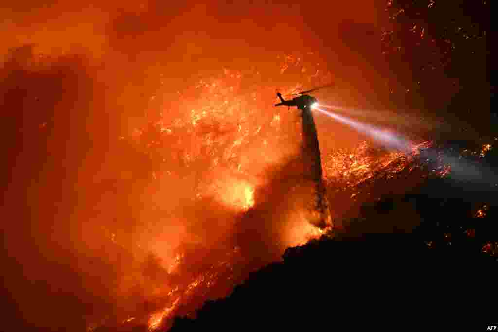 A fire fighting helicopter drops water as the Palisades fire grows near the Mandeville Canyon neighborhood and Encino, California, Jan. 11, 2025. The Palisades Fire, the largest of the Los Angeles fires, spread toward previously untouched neighborhoods, forcing new evacuations and dimming hopes that the disaster was coming under control.