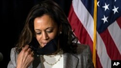 FILE - Democratic vice presidential candidate Senator Kamala Harris, then still the nominee, removes her face mask as she prepares to speak at the Hotel DuPont in Wilmington, Delaware, Aug. 13, 2020.