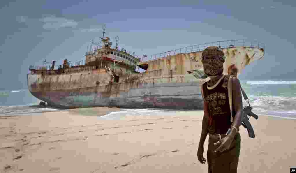 A masked Somali pirate stands near a Taiwanese fishing vessel that washed up on shore after the pirates were paid a ransom and released the crew, in the once-bustling pirate den of Hobyo, Somalia, Sept. 23, 2012.