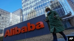 Seorang perempuan yang mengenakan masker berjalan melewati kantor perusahaan e-commerce asal China, Alibaba, di Beijing, pada 13 Desember 2021. (Foto: AP/Andy Wong)