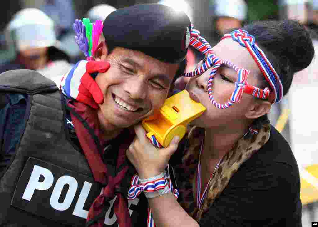 Seorang demonstran anti-pemerintah meniup sebuah peluit raksasa ke seorang petugas polisi anti kerusuhan di luar markas Partai Pheu Thai, Partai Perdana Menteri Yingluck Shinawatra yang saat ini berkuasa, di Bangkok, Thailand.