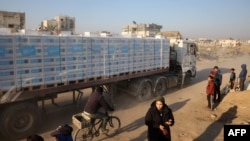 Orang-orang memperhatikan truk bermuatan bantuan kemanusiaan yang melintas di jalan di Khan Younis, selatan Jalur Gaza, 30 Januari 2025. (Foto: Eyad Baba/AFP)
