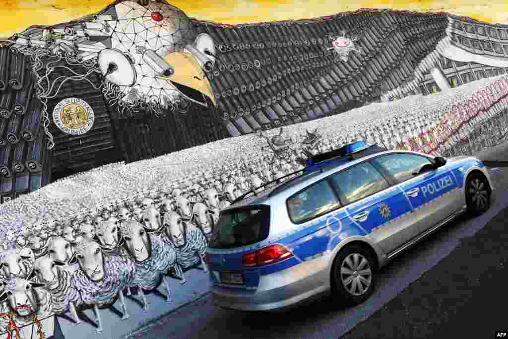 Sebuah mobil polisi Jerman melewati lukisan mural yang menampilkan lambang elang pemerintah Amerika dengan lencana yang bertuliskan sindiran "Badan Keamanan Nasional Seluruh Dunia" di kota Cologne, Jerman Barat.