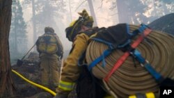Two firefighters from Cosumnes Fire Department carry water hoses while holding a fire line to keep the Caldor Fire from spreading in South Lake Tahoe, Calif., Sept. 3, 2021. 