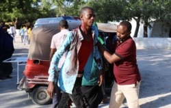 A man assists a civilian injured at the scene of a car bomb explosion at a checkpoint in Mogadishu, Somalia, Dec, 28, 2019.