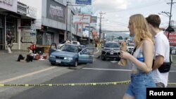 Turistas caminan cerca del lugar donde asaltantes dispararon e hirieron a dos personas que viajaban en un vehículo en la capital San José, el 10 de enero de 2024.
