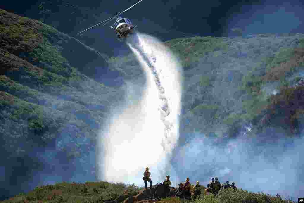 Firefighters watch as a helicopter drops water on a wildfire, in Laguna Beach, California.