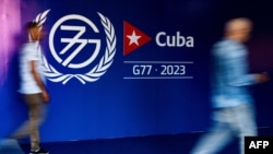 2023年9月13日，哈瓦那新聞發布廳開幕期間，人們走在77國集團+中國峰會的標誌附近. (法新社)