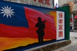 FILE - A tourist, far right, walks by a mural painted on a wall on Taiwan's Kinmen islands, which lie 3.2 kms (2 miles) from the mainland China coast, in the Taiwan Strait, Oct. 21, 2020.