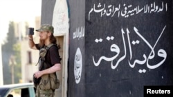 FILE - A militant Islamist fighter uses a mobile to film his fellow fighters taking part in a military parade along the streets of Syria's northern Raqqa province.