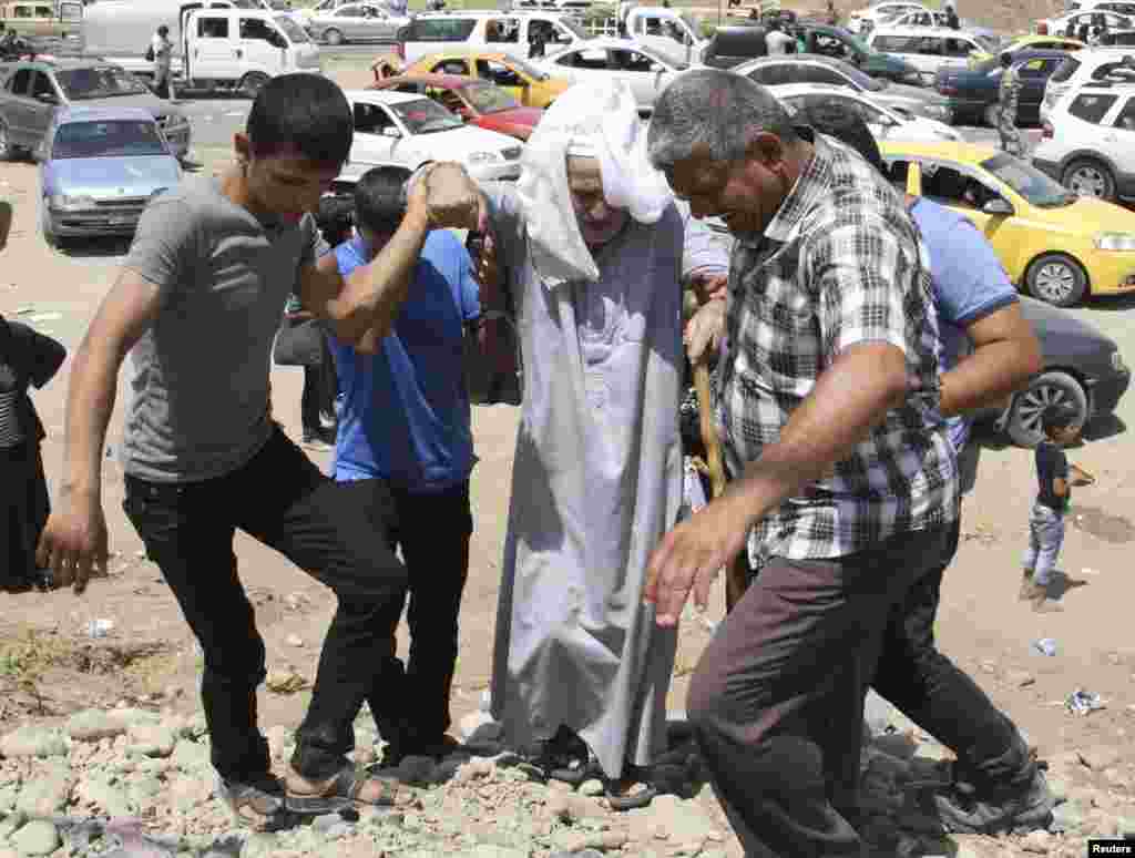 Warga membantu pria lanjut usia saat keluarga-keluarga yang melarikan diri dari kekerasan di Mosul menunggu di pos pemeriksaan di luar kota Irbil, Irak (10/6).