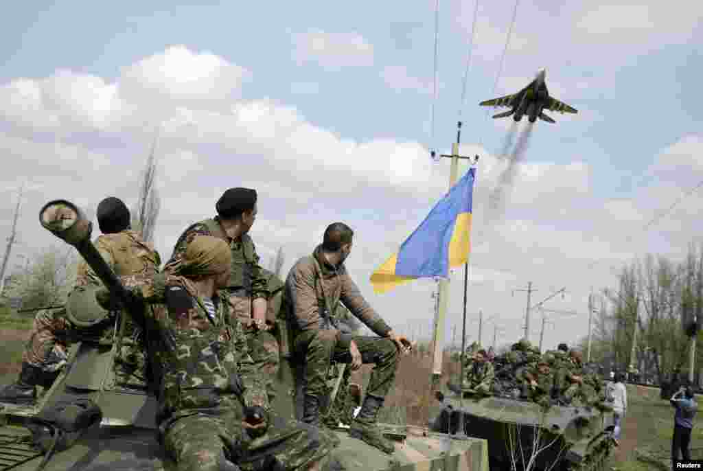 Ukrainian servicemen look at a Ukrainian military jet fly above them while they sit on top of armored personnel carriers in Kramatorsk, Ukraine, April 16, 2014.