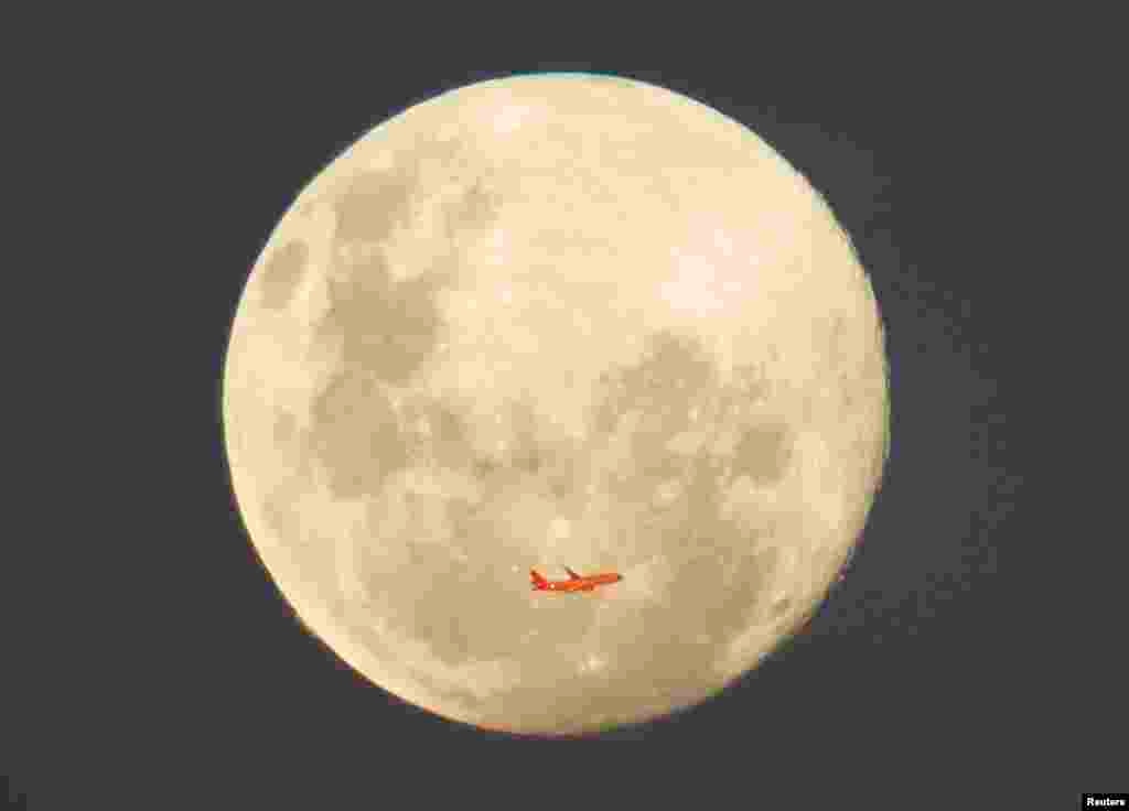 A Virgin Airlines commercial aircraft is illuminated by the setting sun in front of a full moon after taking off from Sydney Airport, Australia.