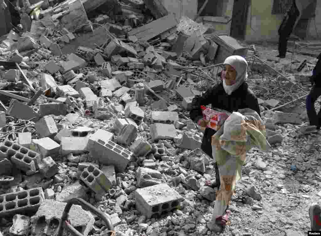 Seorang anak perempuan membawa barang miliknya dan berjalan di reruntuhan gedung yang menurut para aktivis hancur akibat serangan udara yang dilakukan oleh pasukan setia Presiden Suriah Bashar al-Assad di Arbeen, 14 Januari 2014.