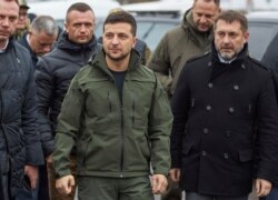 Ukrainian President Volodymyr Zelenskiy, center, visits reconstruction of the bridge crossing over the Siverskyi Donets River, where the local residents cross the delimitation line in Stanitsa village, Luhanska in eastern Ukraine.