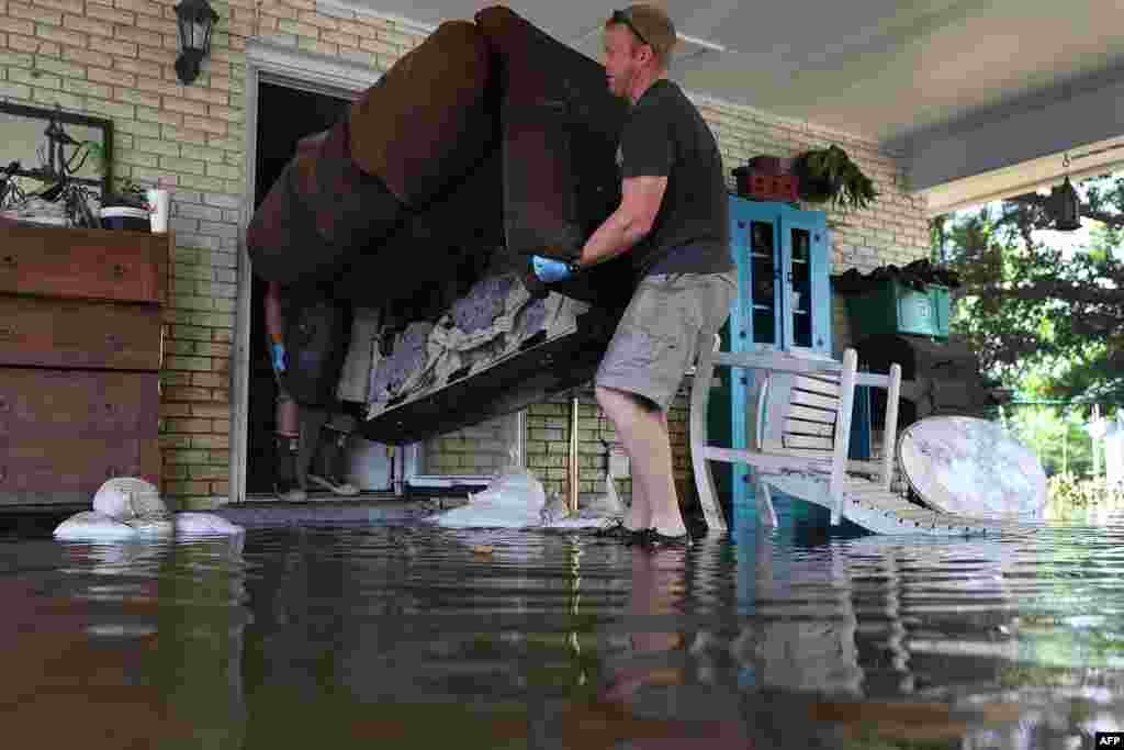 Mike Wroten (L) and Matt Wroten throw a waterlogged couch out of the house as they clear Mike's home out after floodwaters inundated it in St. Amant, Louisiana, Aug. 19, 2016.