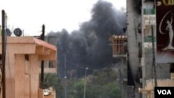 Dua tentara pemberontak Libya terlihat di jalanan Misrata. Asap dari serangan roket masih mengepul di kota ini, Minggu (24/4).