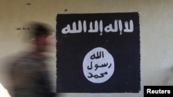 Seorang tentara berjalan melewati bendera hitam yang biasa digunakan oleh militan ISIS.