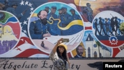 ARCHIVO - Mikia Cain se toma una selfie frente al mural "Igualdad absoluta", que marca el lugar donde un general de la Unión emitió una orden en 1865 que condujo a la libertad de los esclavos en Texas, durante la celebración de Juneteenth en Galveston, el 19 de junio de 2023.