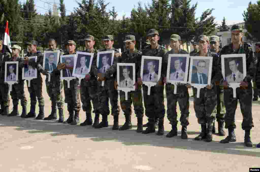 Forces loyal to Syria's President Bashar al-Assad carry pictures of him and his late father, former Syrian president Hafez al-Assad, as they commemorate the 67th anniversary of the founding of the Baath party, at an undisclosed location, April 7, 2014.