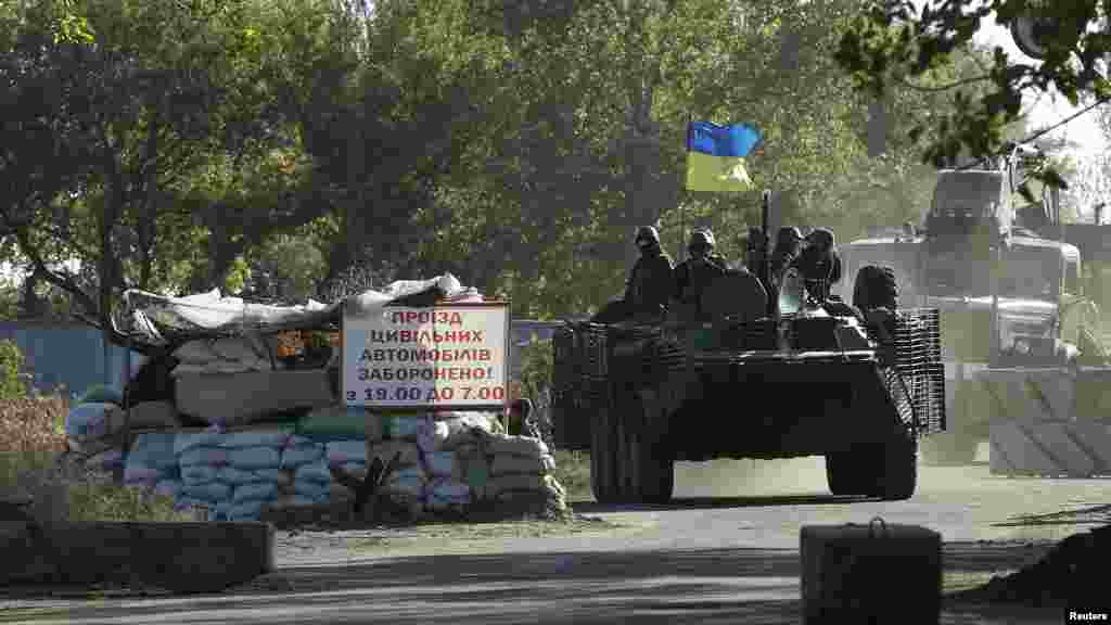 Ukrainian servicemen ride on an armoured vehicle in front of a sign that reads, "The passage of civilian vehicles is prohibited from 19.00 till 7.00," the eastern Ukrainian town of Kramatorsk, Sept. 20, 2014.
