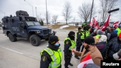 FILE - Protesters interact with police officers who stand guard on a street after Windsor Police said that they are starting to enforce a court order to clear truckers and supporters blocking access to the Ambassador Bridge, which connects Detroit and Win
