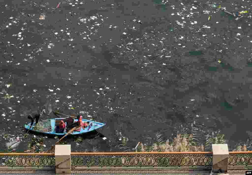 A man rows a fishing boat in the plastic-filled Nile river water off the shore in the Egyptian capital's twin city of Giza.
