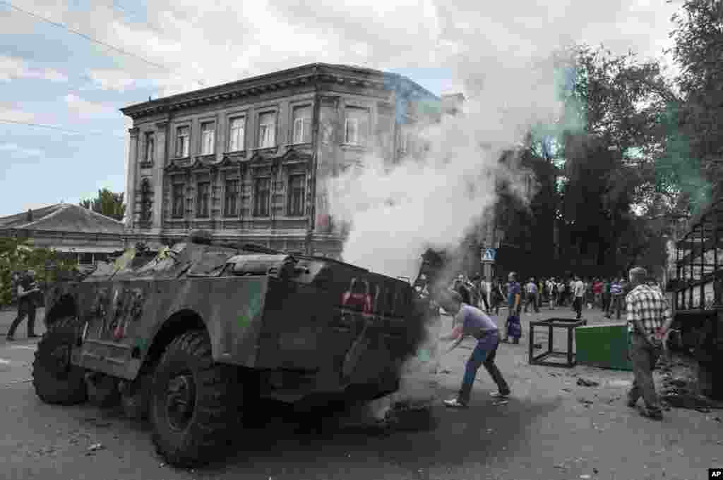 Penduduk lokal tampak di sekitar sebuah kendaraan militer yang terbakar di lokasi pertempuran antara pasukan Ukraina dan pejuang Pro-Rusia di Mariupol, di wilayah timur Ukraina. 