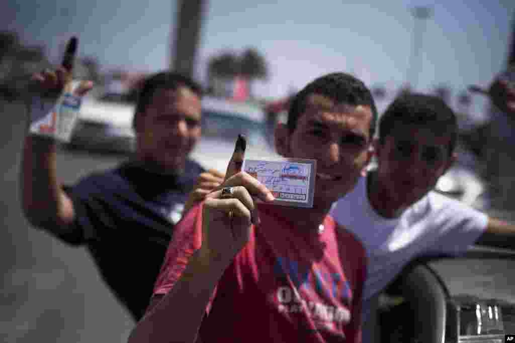 Libyan men hold their elections ID cards while celebrating election day in Tripoli, Saturday, July 7, 2012.