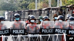 Truk militer beserta tentara di dalamnya diparkir di belakang polisi penjaga keamanan di belakang barikade jalan di Mandalay, Myanmar, 19 Februari 2021. (Foto: AP/ File)
