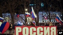 Orang-orang mengibarkan bendera nasional Rusia untuk merayakan, di pusat Donetsk, wilayah yang dikuasai oleh militan pro-Rusia, Ukraina timur, Senin malam, 21 Februari 2022. (Foto: AP)