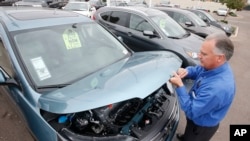 FILE - A sales manager at a Honda car dealership opens the hood of a Honda CRV SUV in Tempe, Arizona, Dec. 2, 2014.