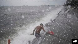 Ombak mengenai seorang warga Filipina ketika mengambil sandal karetnya di Manila Bay, Filipina, 10 Mei 2015.