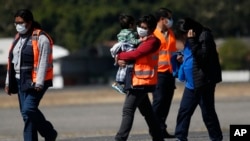 FILE - In this March 12, 2020 file photo, an immigration worker carries a young Guatemalan migrant deported from the U.S., at La Aurora International airport in Guatemala City.