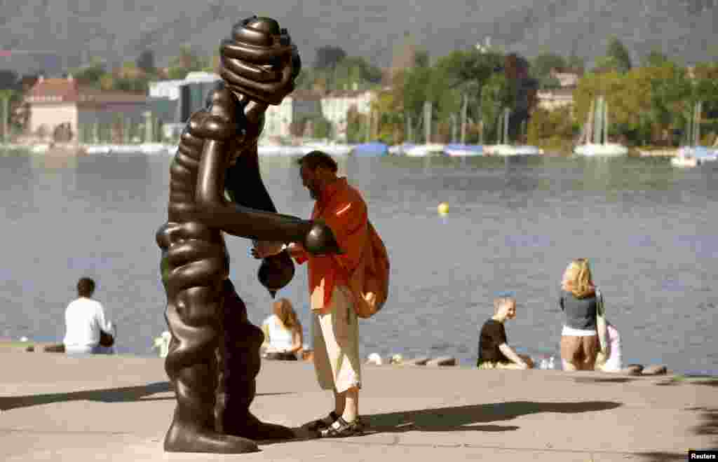 A man stands beside a sculpture of the group 'Vier Grosse Geister' (Four Big Ghosts') from 2003 by German artist Thomas Schuette on the shore of Lake Zurich in Zurich, Switzerland.