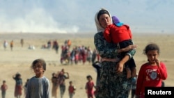 FILE - Displaced people from the minority Yazidi sect, fleeing violence from forces loyal to the Islamic State in Sinjar, walk toward the Syrian border near the town of Elierbeh, Aug. 11, 2014.