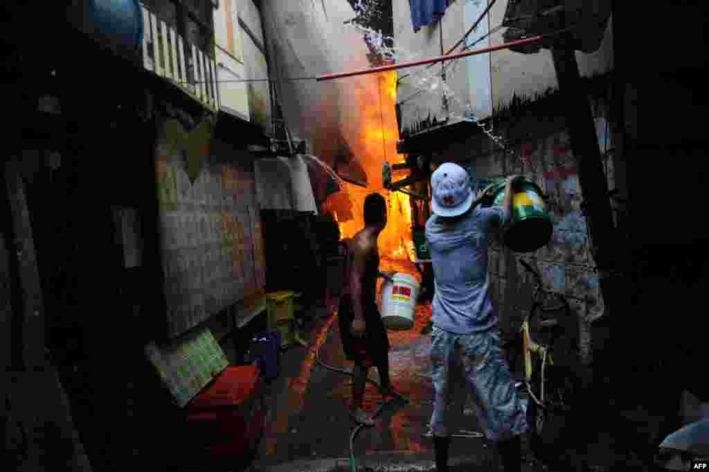 Seorang warga menggunakan ember berisi air untuk memadamkan api setelah kebakaran melanda sebuah kawasan kumuh di Manila, Filipina.