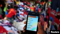 Mwanaume akiinua simu yake ya mkononi inayoonyesha ukurusa wa M-Pesa wa kutuma na kupokea pesa kwa mpiga picha, katika soko la mtaa wa Kibera, mjini Nairobi, Disemba 31, 2014