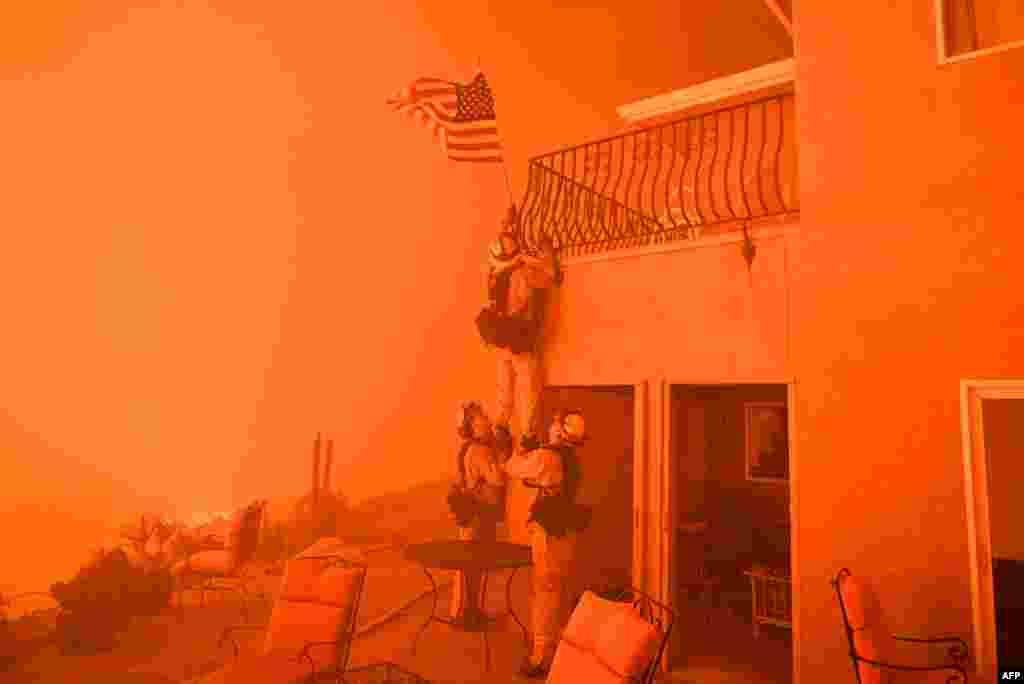 Firefighters remove a U.S. flag as flames from the "Wall Fire" close in on a luxury home in Oroville, California, July 8, 2017.
