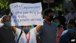 Seorang perempuan berunjuk rasa dengan membawa kertas bertuliskan bahasa Spanyol "Saya seorang perawat.Saya berjuang untuk (menyelamatkan)mu dan diriku sendiri. Tinggallah di rumah!" di Mexico City, Senin (13/4).