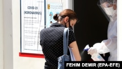 A medical staff attends to a woman as she arrives to test for coronavirus, at a hospital in Sarajevo, Bosnia and Herzegovina, 08 July 2020. 
