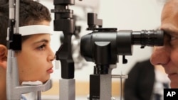 FILE - Dr. Albert Maguire checks the eyes of Misa Kaabali, 8, at Children's Hospital of Philadelphia, Oct. 4, 2017. Misa was 4 when he received his gene therapy treatment. On Dec. 19, 2017, the Food and Drug Administration approved therapy that improves t