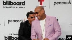 Randy Malcolm Martínez, izquierda, hace el gesto de morder el hombro de Alexander Delgado a la llegada del dúo cubano Gente de Zona a la alfombra azul de los Premios Billboard de la Música Latina en Coral Gables, Florida, el jueves 5 de octubre de 2023. 